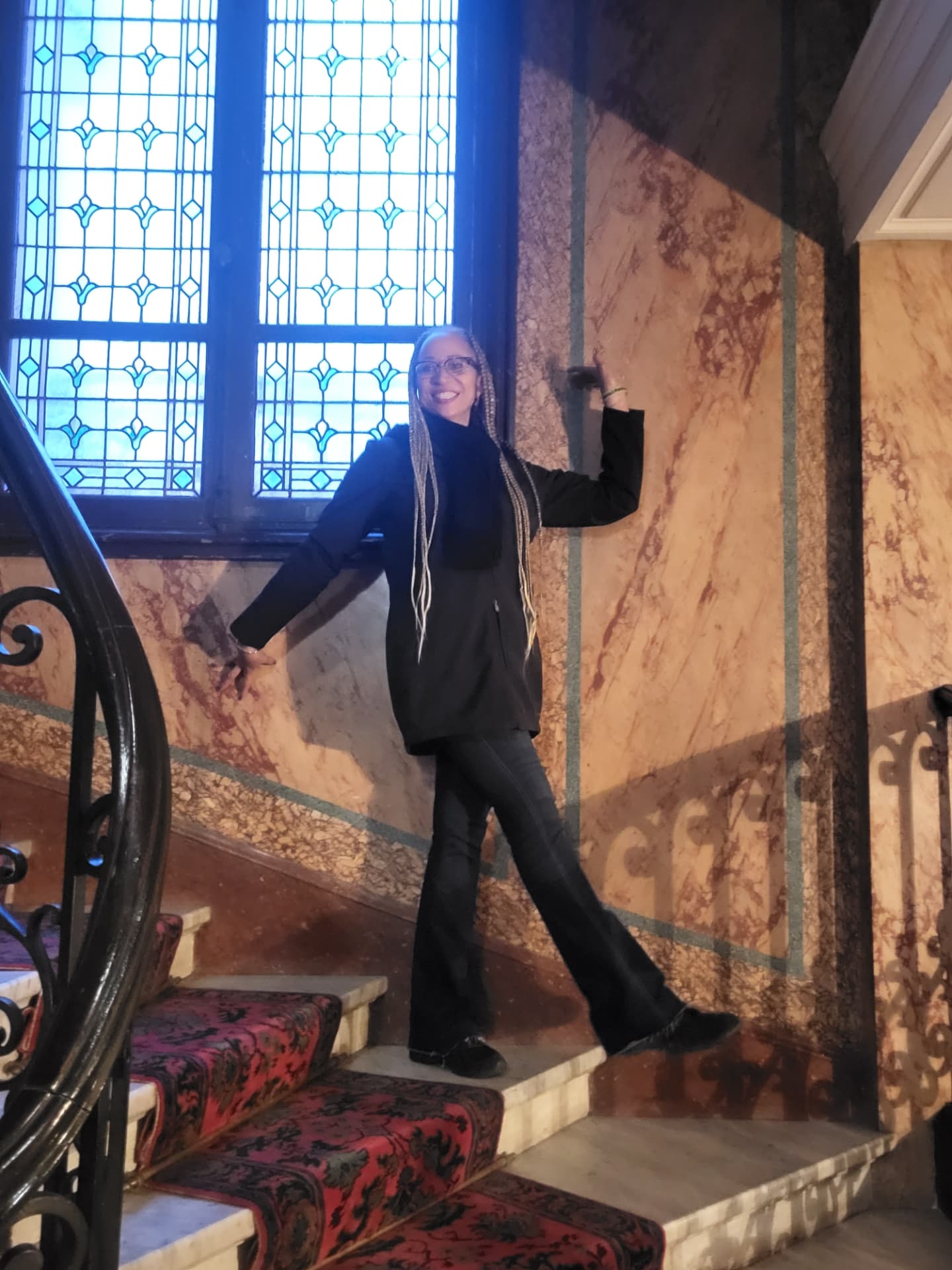Allison posing playfully on a marble staircase beneath a blue stained-glass window