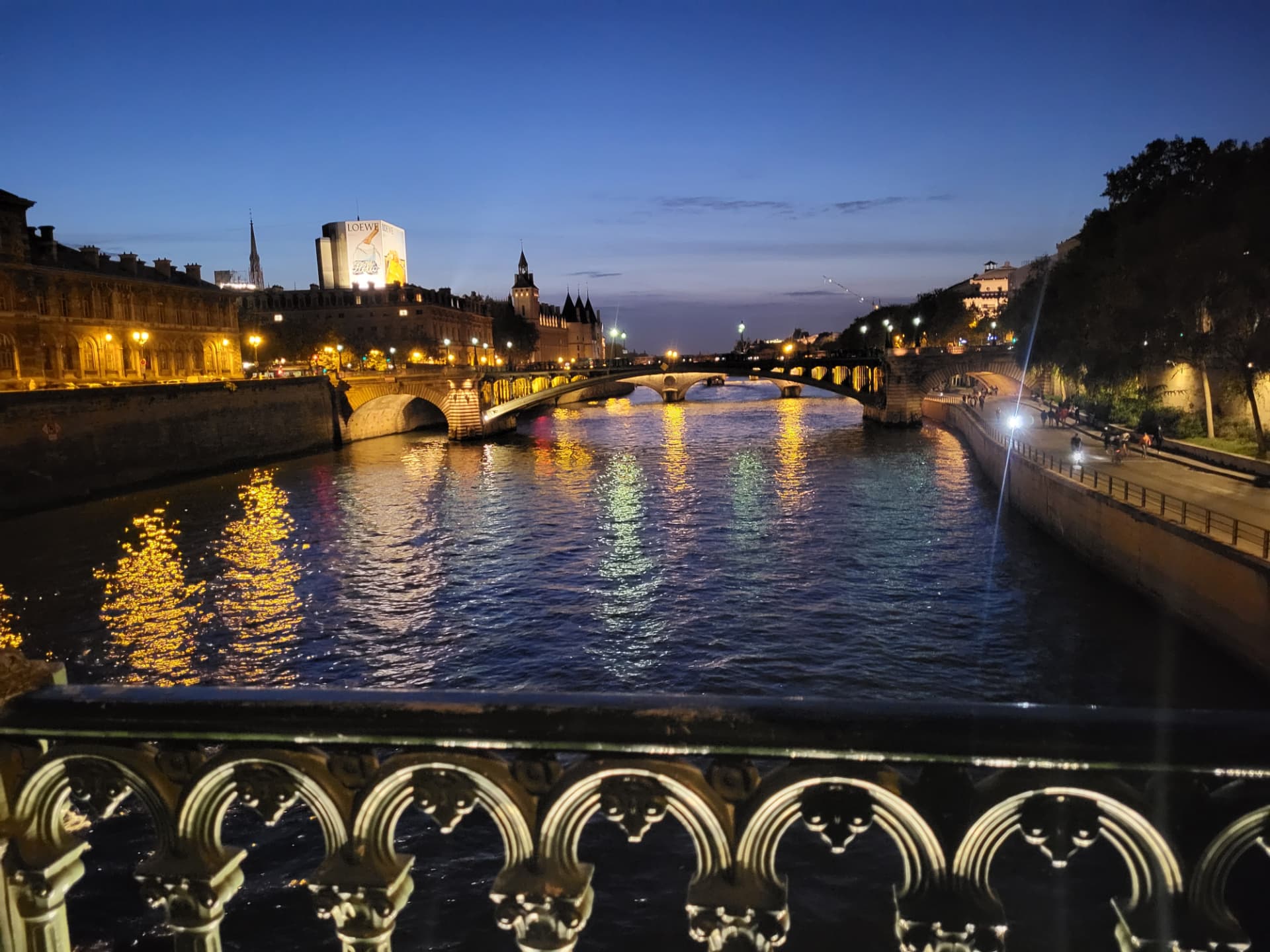 The Seine at dusk, lit bridges reflected in the water beyond an ornate iron railing