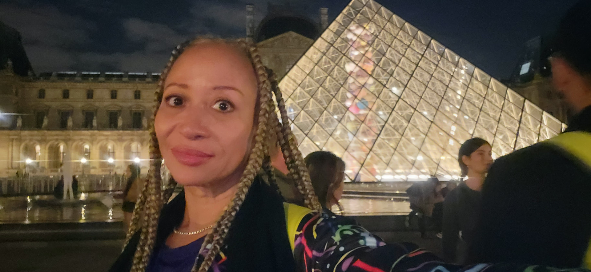 Allison with long braids in front of the illuminated Louvre pyramid at night