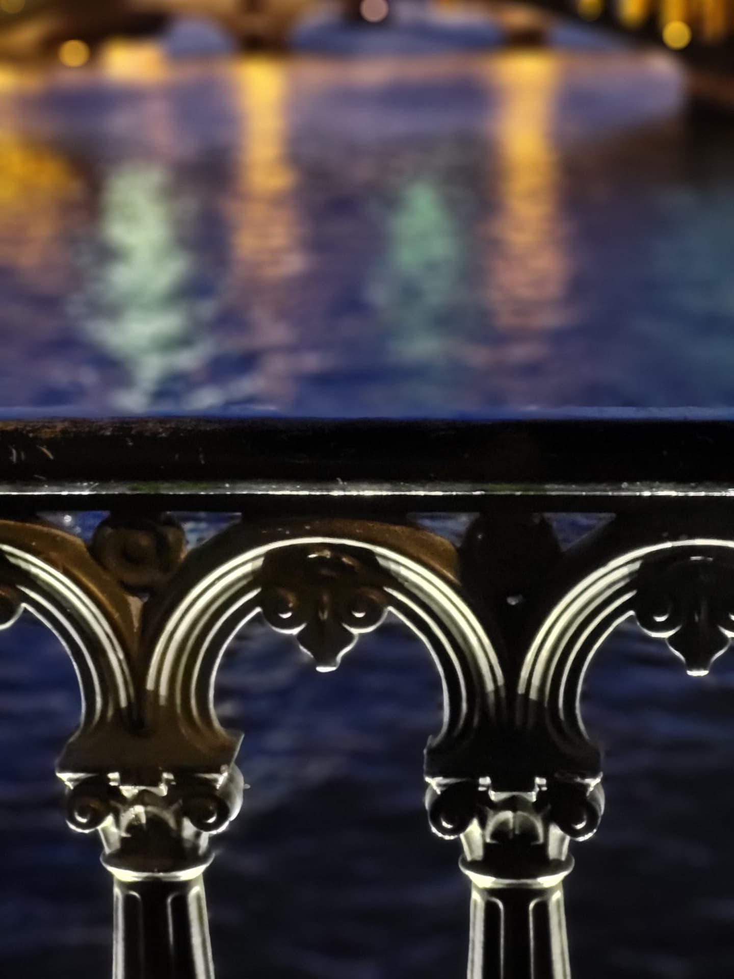Close-up of an ornate iron bridge railing above the softly blurred, glowing Seine