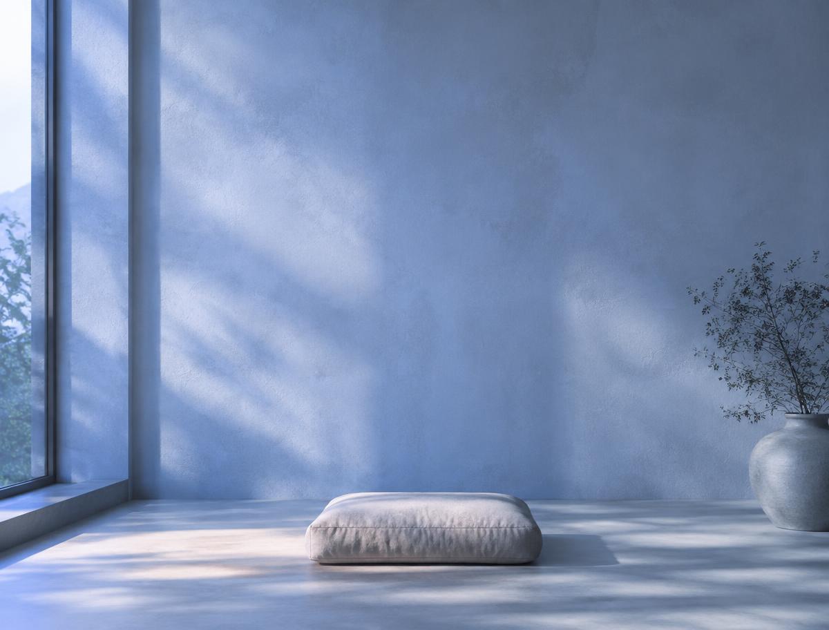 Empty meditation room with soft blue morning light and a single linen cushion